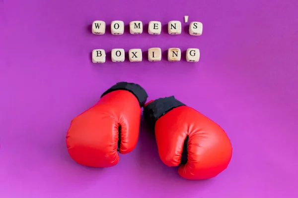 Red boxing gloves on a pink background and the inscription made of wooden beads \