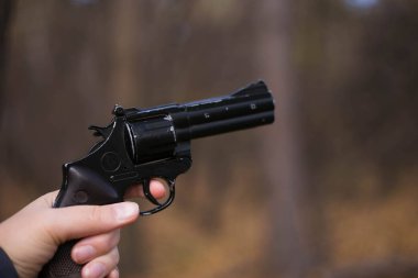 Kasvetli bir ormanın arka planında silah tutan bir el. Kadın eli tabanca