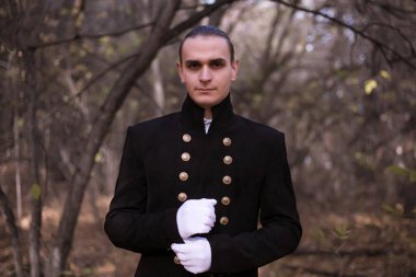 19. yüzyıl kıyafetleri içinde, kasvetli bir ormanda beyaz eldivenler giyen bir adam..
