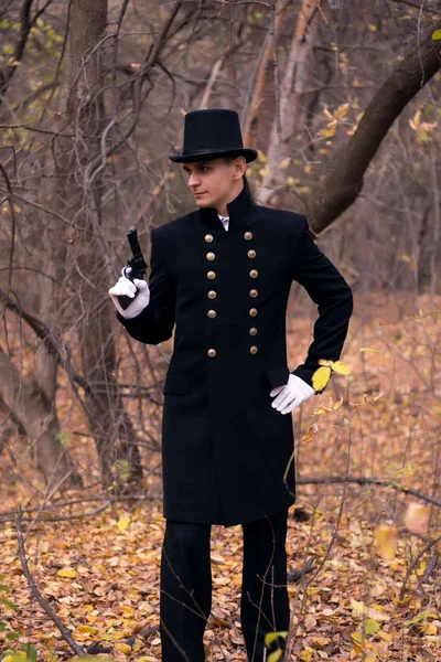 A man with a gun in the clothes of the nineteenth century in a gloomy forest.