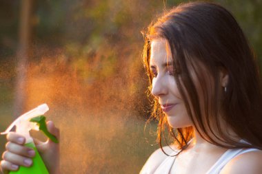 Young woman spraying water on herself from a spray bottle, close-up.