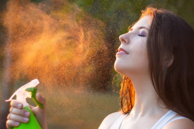 Young woman spraying water on herself from a spray bottle, close-up.