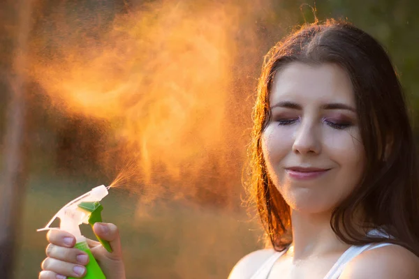 Mujer joven rociando agua sobre sí misma de una botella de spray, primer plano . — Foto de Stock