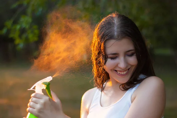 Mujer joven rociando agua sobre sí misma de una botella de spray, primer plano . — Foto de Stock