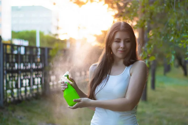 Mujer joven rociando agua sobre sí misma de una botella de spray en un parque de verano . — Foto de Stock