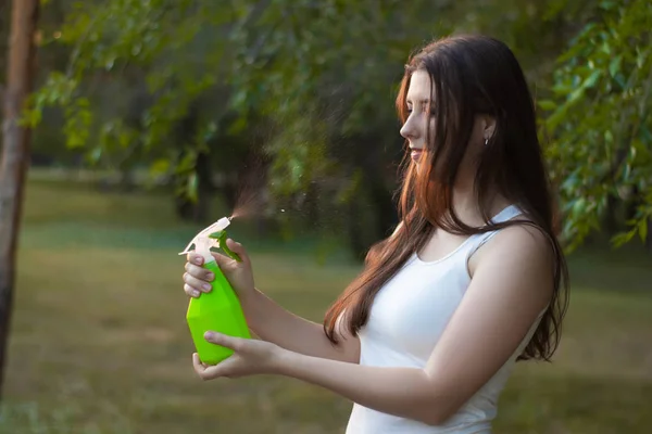 Mujer joven rociando agua sobre sí misma de una botella de spray en un parque de verano . — Foto de Stock