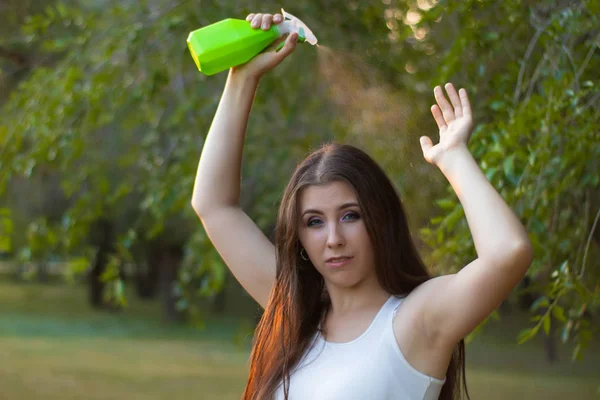 Mujer joven rociando agua sobre sí misma de una botella de spray en un parque de verano . — Foto de Stock