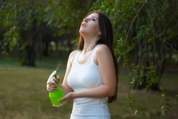 Młoda kobieta spryskuje się wodą z butelki w parku letnim. — Zdjęcie stockowe