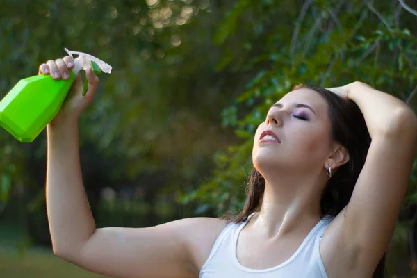 Mujer joven rociando agua sobre sí misma de una botella de spray en un parque de verano . — Foto de Stock