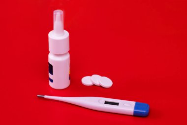 Elektronik termometre, sprey ve kırmızı arka planda haplar. Grip ve soğuk algınlığı tedavisinde kullanılır..