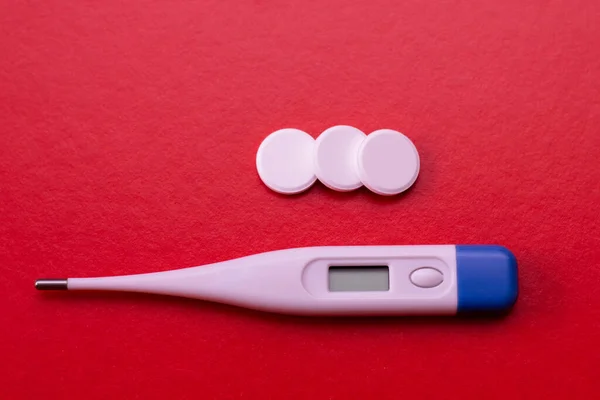 Elektronische thermometer en pillen op een rode achtergrond. Middelen voor de behandeling van griep en verkoudheid, verlaging van de temperatuur. — Stockfoto