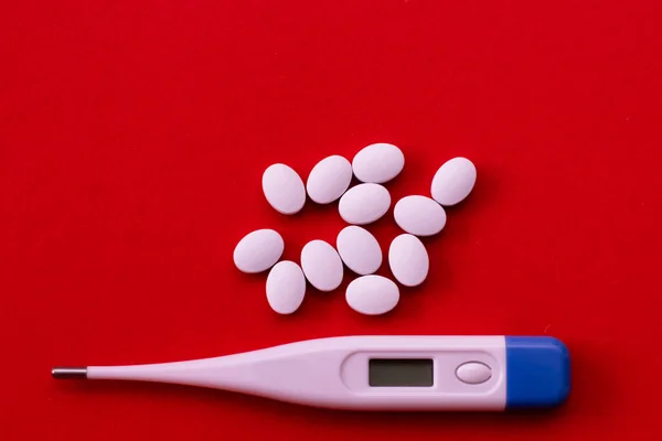 Elektronische thermometer en pillen op een rode achtergrond. Middelen voor de behandeling van griep en verkoudheid, verlaging van de temperatuur. — Stockfoto