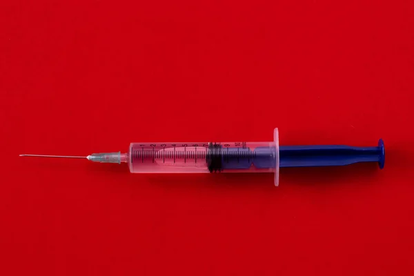 Spritze mit Medikamenten auf rotem Hintergrund. Die Behandlung der Krankheit, der Kampf gegen das Virus. — Stockfoto