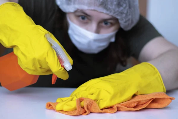 Disinfection of surfaces in everyday life. Hands in rubber gloves wipe the furniture. Focus on hands, face in the background in defocus, the photo