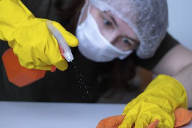 Günlük hayatta yüzeylerin dezenfekte edilmesi. Lastik eldivenli eller mobilyaları siler. Ellere odaklan, arka plana odaklan.