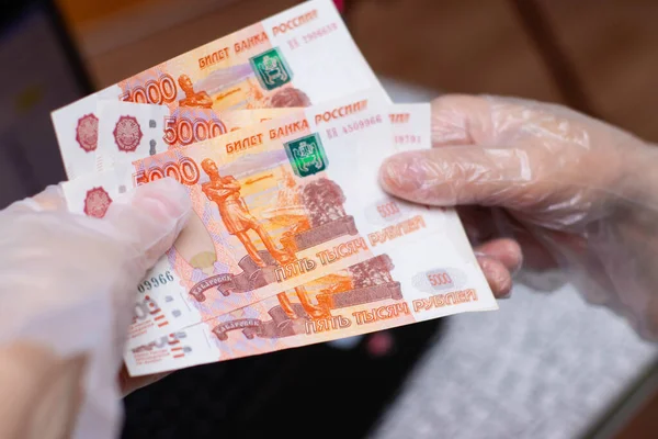 Koruyucu tek kullanımlık eldivendeki bir el, para transferleri, Rus rublesi. Koronavirüs salgını sırasında alınan önlemler, fotoğraf...