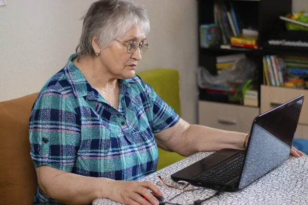 An older woman sits at a laptop. Mastering the older generation of technology by people. Internet communication from home