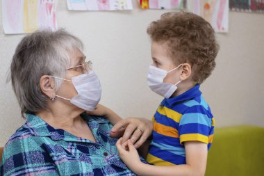 Koruyucu tıbbi maskeli büyükanne ve torun. Salgın sırasında karantina, eski neslin korunması, akrabalarla iletişim, fotoğraf...