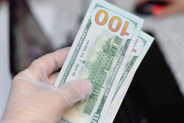 Tek kullanımlık koruyucu eldivendeki bir el dolar tutar. Koronavirüs salgını sırasında alınan önlemler.