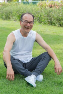 Asyalı yaşlı adam gülümseme ve parkta çim oturmak. Mutluluk, rahatlatıcı.