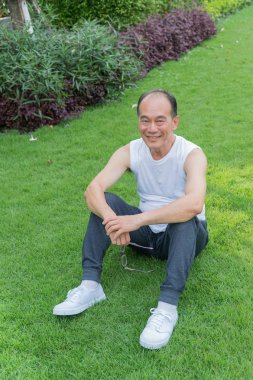 Asyalı yaşlı adam gülümseme ve parkta çim oturmak. Mutluluk, rahatlatıcı.