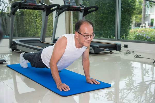senior man on blue mat exercising by doing push ups in the fitness center or gym, sport and health concept.
