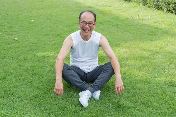 Asyalı yaşlı adam gülümseme ve parkta çim oturmak. Mutluluk,