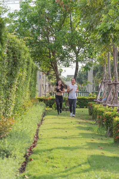 yaşlı adam ve kadın parkta koşu egzersiz, gülümseyerek ve açık çimenlerin üzerinde çalışan.