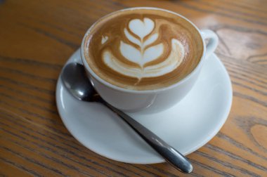 Kalp desenli ahşap arka plan, Sıcak karamel latte üzerinde beyaz bir fincan kahve