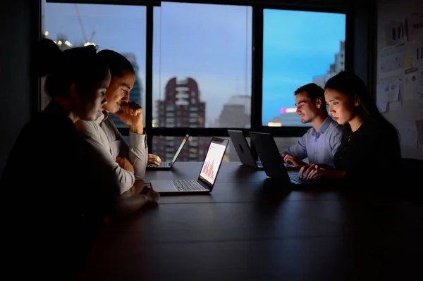 Бізнес-команда, що працює з комп'ютером понаднормово вночі і низьким освітленням — стокове фото