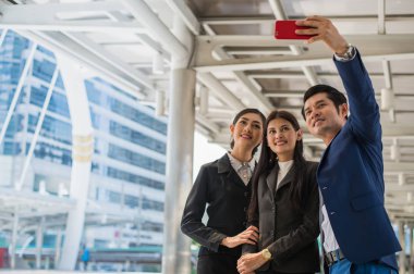 Asian business team  taking a selfie with smartphone in the city clipart