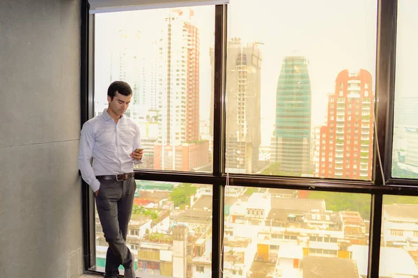 Hombre de negocios guapo usando teléfono inteligente responder a los mensajes cerca de la ventana y copiar el espacio para el texto . — Foto de Stock