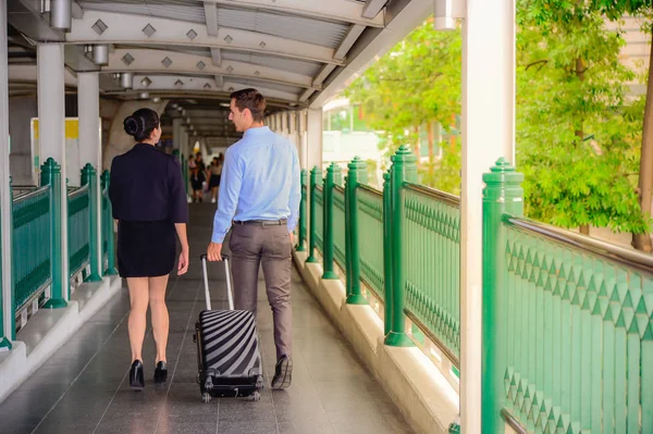 Hombre de negocios y mujer de negocios hablar y caminar junto con el equipaje negro en la calle pública, viajes de negocios — Foto de Stock