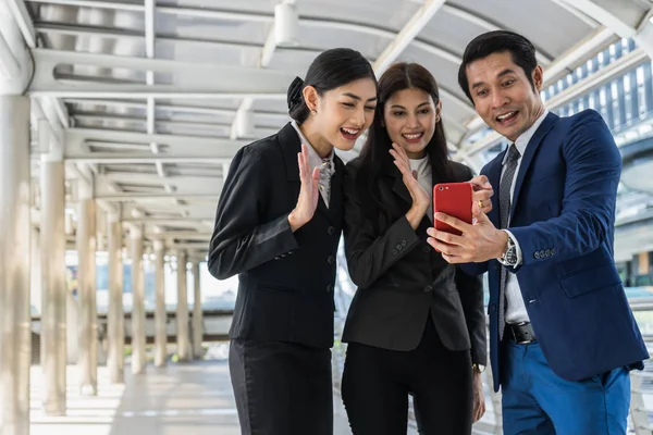 Asya iş adamı ve iş kadını biri üstünde hareket eden telefon ile konferans görüşmesi yapıyor