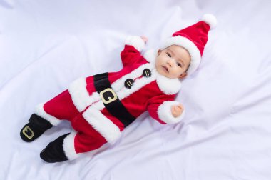 Kırmızı Noel Baba kostümü giyen küçük bebek beyaz kürk halıda uyuyor. Noel ve Yeni Yıl tatili kutlaması kavramı.