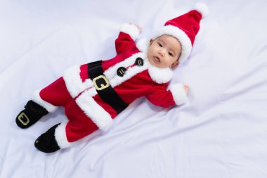 Kırmızı Noel Baba kostümü giyen küçük bebek beyaz kürk halıda uyuyor. Noel ve Yeni Yıl tatili kutlaması kavramı.
