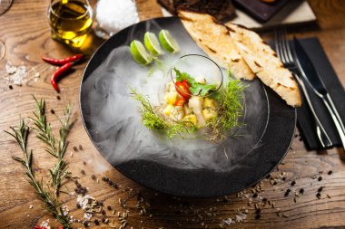 Scallop ceviche siyah kasede sıvı buz dumanıyla servis edilir