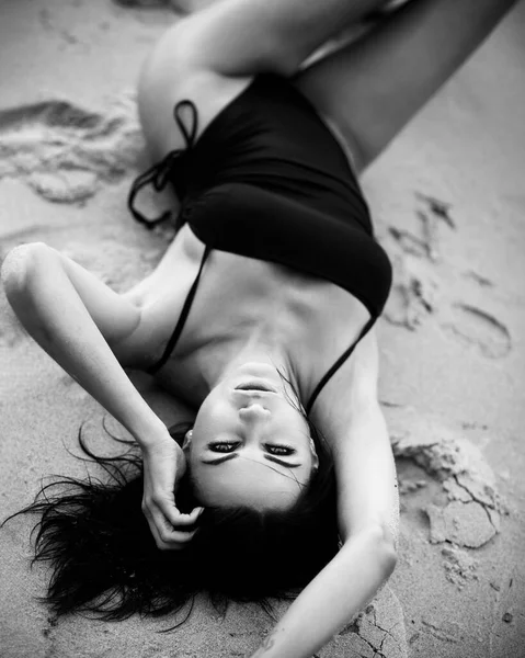 Beautiful lady in black swimsuit lies on a sandy beach