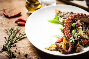 Sıcak ahtapot salatası, kızarmış sebzeler ve beyaz tabakta ji sosu. Lezzetli, sağlıklı, geleneksel deniz ürünleri öğle yemeği için masaya servis edilir..