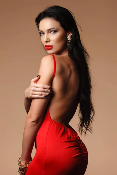 Sieraden en schoonheid concept. mooi brunette dame portret in moderne edelstenen en rode jurk op naakte achtergrond. Vrouw staande en demonstrerende schouder en rug — Stockfoto