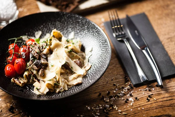 Pasta de pappardelle Angus negra con carne de res, champiñón y queso parmegano en un plato negro. Delicioso primer plano mediterráneo de comida tradicional servido para el almuerzo en el restaurante gourmet cocina moderna . — Foto de Stock