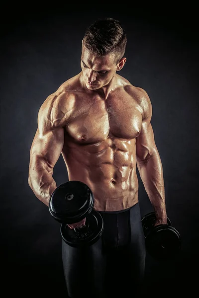 Fitness en gimnasio, deporte y estilo de vida saludable. Hombre atlético guapo mostrando su cuerpo entrenado sobre fondo negro. Culturista modelo masculino entrenamiento bíceps músculos con mancuerna . — Foto de Stock