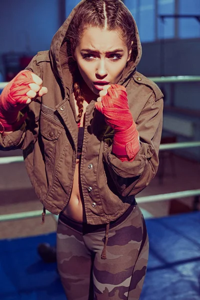 Sport, fitness concept. Portrait of female boxer in sport wear with fighting stance against spotlight. Sexy fitness blonde girl in sport wear with perfect body in the boxing gym posing in boxing ring
