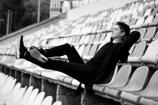 Guy Dark Clothes Sits Contentedly Empty Stadium Monochrome Photo — Free Stock Photo
