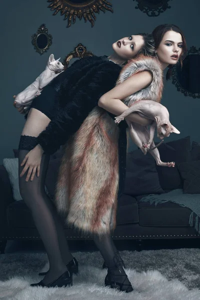 Models in fur coats with cats sphinx posing on camera