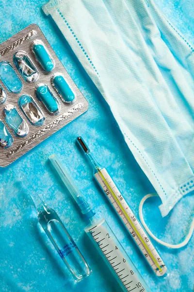 Healthcare and medicine. Mask, thermometer, drugs, pills, flask with liquid, syringe closeup. Coronovirus COVID-19 concept. Vertical Flat lay photo.