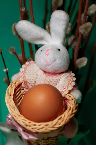 Toy rabbit holds a chicken egg in a basket. Easter bunny with egg