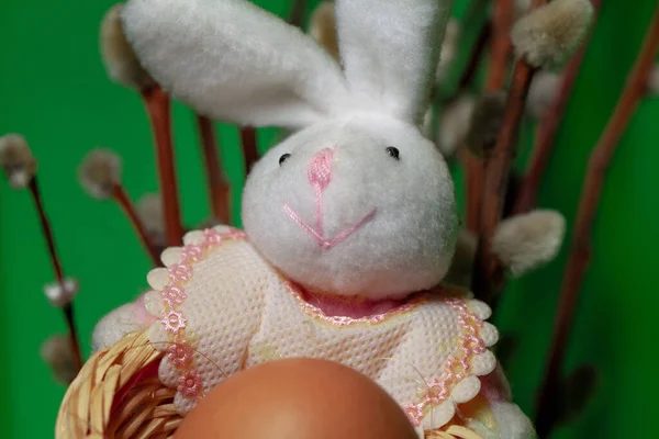 Toy rabbit holds a chicken egg in a basket. Easter bunny with egg