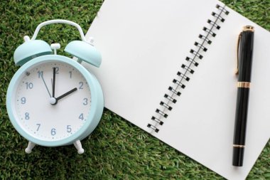 Alarm saati ve çimen arkaplanı üzerine not defteri