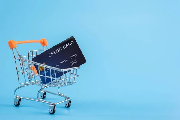 Carrinho de compras com cartão de crédito em fundo azul — Fotografia de Stock